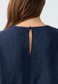 Top in lino blu navy con apertura a chiave sul retro, rifinita con un piccolo bottone. Texture liscia con un leggero lucido.