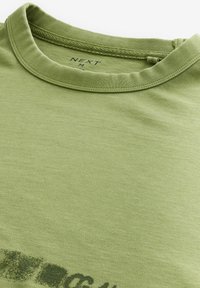 Grøn t-shirt med rund halsudskæring, prydet med et trykt design i en mørkere nuance. Stoffet ser blødt og glat ud.
