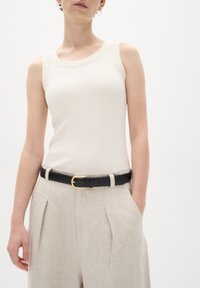 Ljust beige ribbat linne med en bred halsringning, kombinerat med ljusa linnebyxor och ett svart bälte med ett guldspänne.