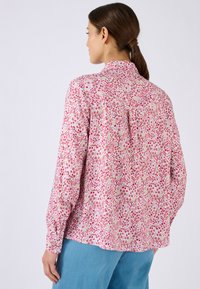 Blusa floral en rosa con mangas cortas y sueltas y una espalda drapeada. Presenta un estampado de flores rojas y amarillas sobre un fondo claro.