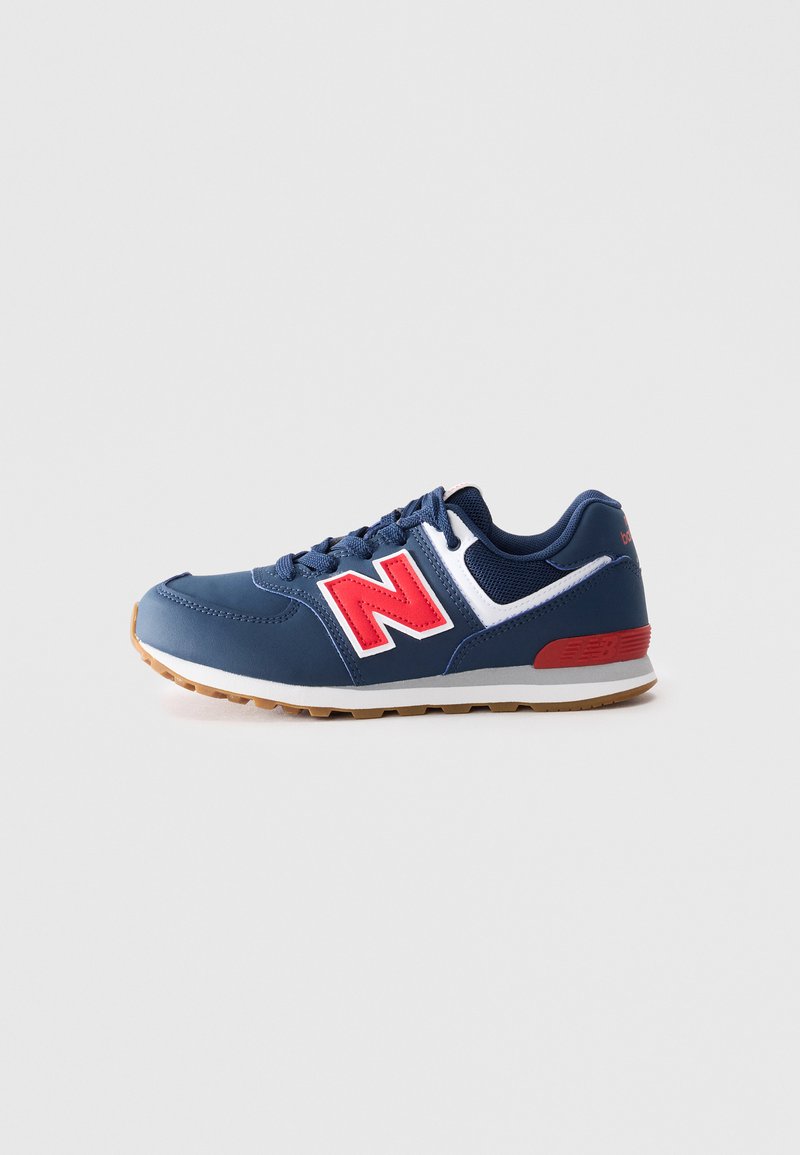 Sneaker New Balance bleu, blanc et rouge avec lacets, semelle en caoutchouc, et tissu en maille et cuir, présenté en profil latéral sur un fond neutre.
