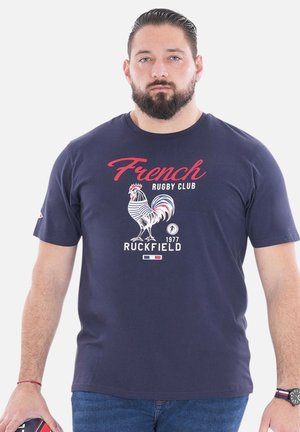 T-shirt bleu marine mettant en avant un graphisme de coq, le texte "French Rugby Club" et "Ruckfield 1977". Tissu en coton avec un col rond et des manches courtes.