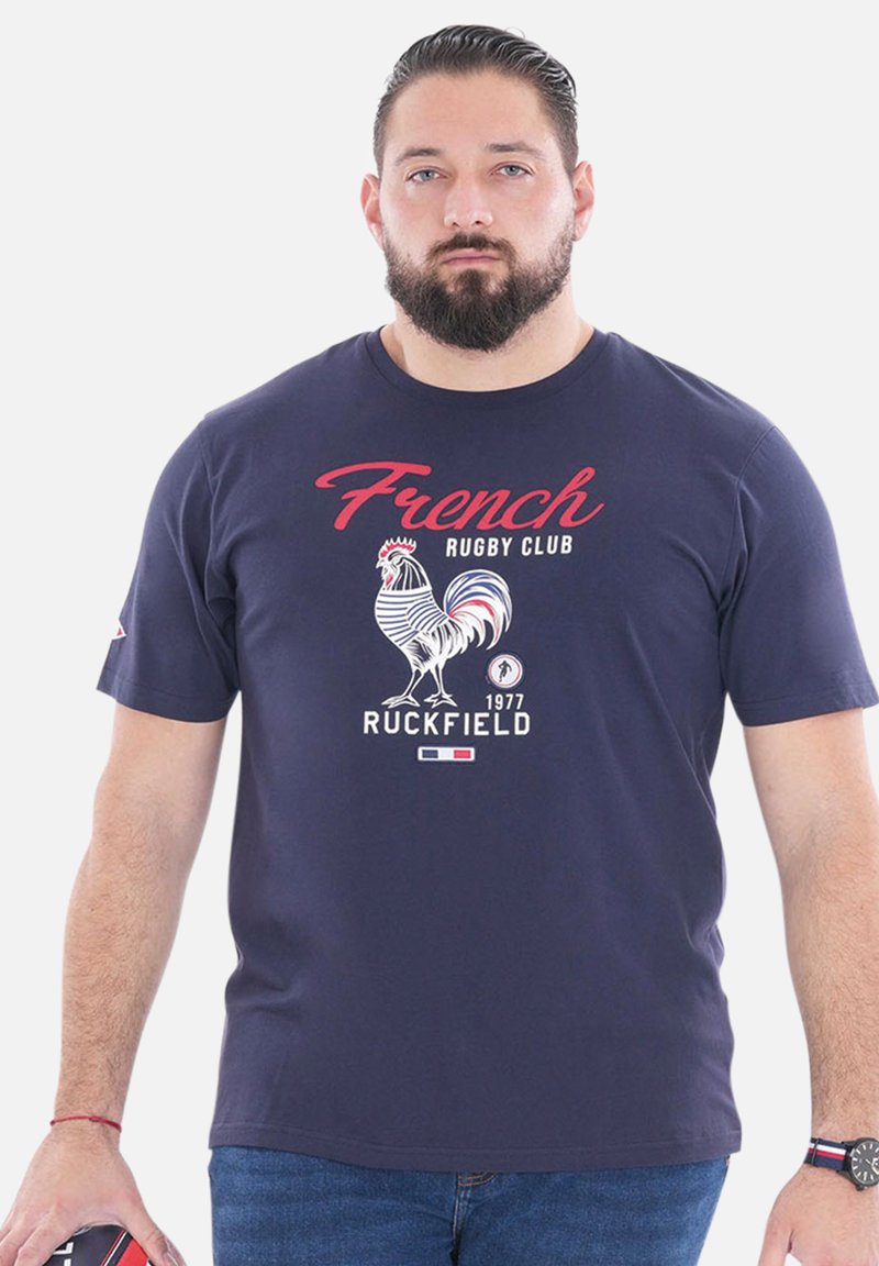 T-shirt bleu marine mettant en avant un graphisme de coq, le texte "French Rugby Club" et "Ruckfield 1977". Tissu en coton avec un col rond et des manches courtes.
