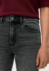 Jean en denim noir taille haute avec une texture lisse, design à cinq poches et couture contrastée, associé à un haut à manches courtes bordeaux.