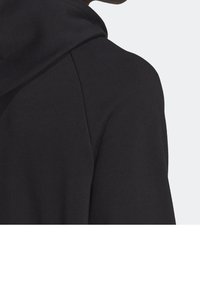 Svart hoodie med hög krage och ett mjukt, texturerat tyg. Designen inkluderar en stor huva och åtsittande ärmar för komfort.