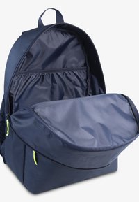 Sac à dos marine avec une forme structurée, comprenant un grand compartiment principal, une poche intérieure et des accents de zip verts. Texture de tissu lisse.