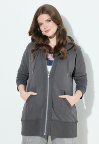 Gray zip-up hoodie with a hood, featuring two front pockets and ribbed cuffs. Soft fabric with a slightly textured surface.