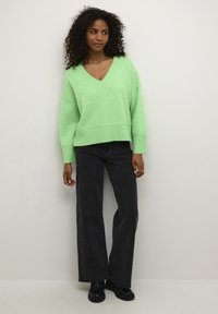 Mintgrüner, übergroßer Pullover mit V-Ausschnitt, geripptem Saum und hochgekrempelten Ärmeln, kombiniert mit schwarzen weiten Jeans und schwarzen Schuhen.