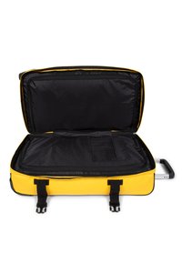 Valigia gialla con un esterno rigido, apertura con zip, rivestimento interno nero, due manici neri e un manico estraibile per un facile trasporto.
