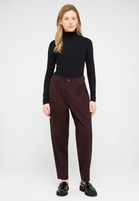 Black ribbed turtleneck paired with dark burgundy high-waisted trousers, featuring front pockets and a single button closure. Black shoes.