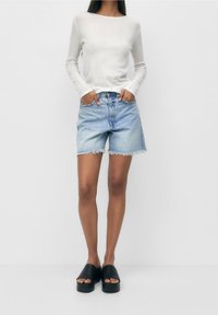 Top de manga larga gris claro, pantalones cortos de mezclilla en azul claro con dobladillo deshilachado y sandalias de plataforma negras. Conjunto simple y casual con colores básicos.