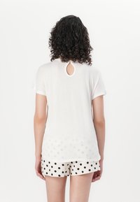 White short-sleeve shirt with a keyhole back detail, paired with polka dot shorts in cream and black. Lightweight and relaxed fit.