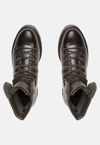 Hnědé kožené turistické boty s polstrovaným límcem, kovovými otvory na tkaničky a texturovanou podrážkou pro lepší přilnavost. Vnitřek vyložený měkkým materiálem.