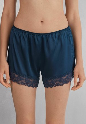 Marina satin shorts med elastiskt midjeband, med en scalloped spetsdetalj längs bottenkanten för extra detalj och textur.
