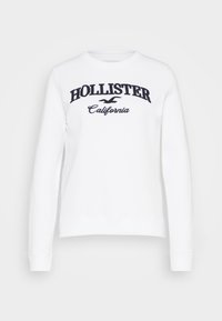 Sudadera blanca de manga larga, con puños y dobladillo acanalados. Presenta bordados con las palabras "HOLLISTER" y "California" en azul marino oscuro. Material suave.
