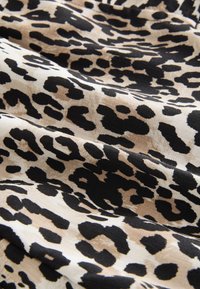 Tkanina w panterkę z czarnymi i beżowymi wzorami na miękkim, teksturowanym materiale. Wzór zawiera nieregularne plamki i kształty.
