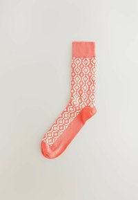Calcetín color coral con un patrón de diamantes blancos, con una textura de punto y un puño sólido en coral. Hecho de un tejido elástico para mayor comodidad.