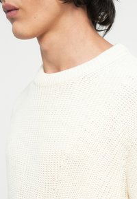 Vit stickad tröja med ribbat, runt halsringning och strukturerad tyg. Designen har ett löst stickat mönster och mjuk finish.