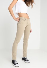 Beige skinny džíny s středně vysokým pasem, pěticí kapsami a kontrastním šitím; kombinované s černými vysokými teniskami.