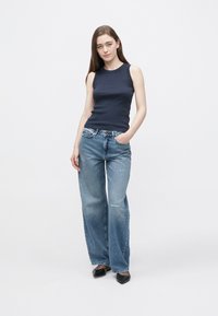 Granatowy top bez rękawów w połączeniu z jasnoniebieskimi dżinsami o szerokich nogawkach, z przetarciami i głębokimi kieszeniami. Stylizację uzupełniają czarne buty w szpic.