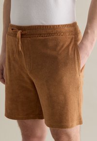 Pantalones cortos de forro polar marrones con cinturilla elástica y cordón; cuentan con bolsillos laterales y un acabado suave y texturizado.