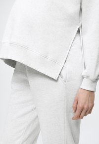 Ανοιχτό γκρι αθλητικό φούτερ με ριμπ μανσέτες, πλαϊνές σχισμές και ταιριαστό παντελόνι με πλαϊνές τσέπες και υφασμένη υφή.