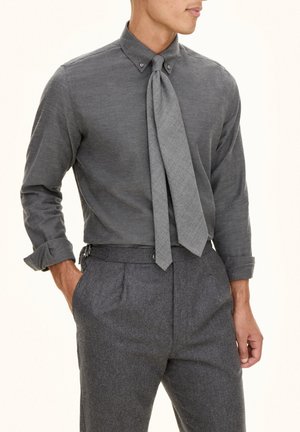 La camicia grigia con bottoni presenta un tessuto strutturato con una cravatta. Abbina pantaloni grigi su misura, che evidenziano un taglio classico e dettagli curati.