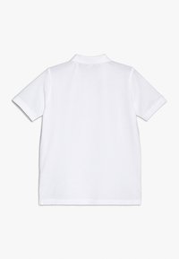 Bílá polo košile s krátkým rukávem, klasickým límečkem, měkkou texturou látky a rovnými lemy bez viditelných log nebo vzorů.