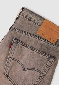 Πίσω τσέπη ξεθωριασμένου γκρι τζιν Levi's 501 με εμφανή ραφές, κόκκινη ετικέτα Levi's και καφέ δερμάτινη ετικέτα με το μέγεθος W32 L32.