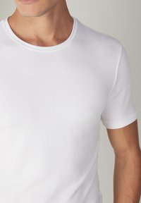 T-shirt blanc à manches courtes en tissu de coton doux, avec un col rond et une texture lisse agrémentée de détails de couture subtils.