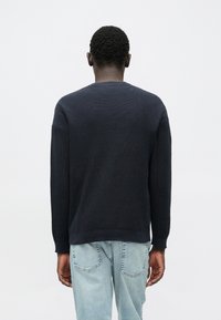 Marineblå strikket sweater med rund halsudskæring og ærmer i fuld længde, kombineret med lyseblå denimjeans. Materialet virker let og tekstureret.