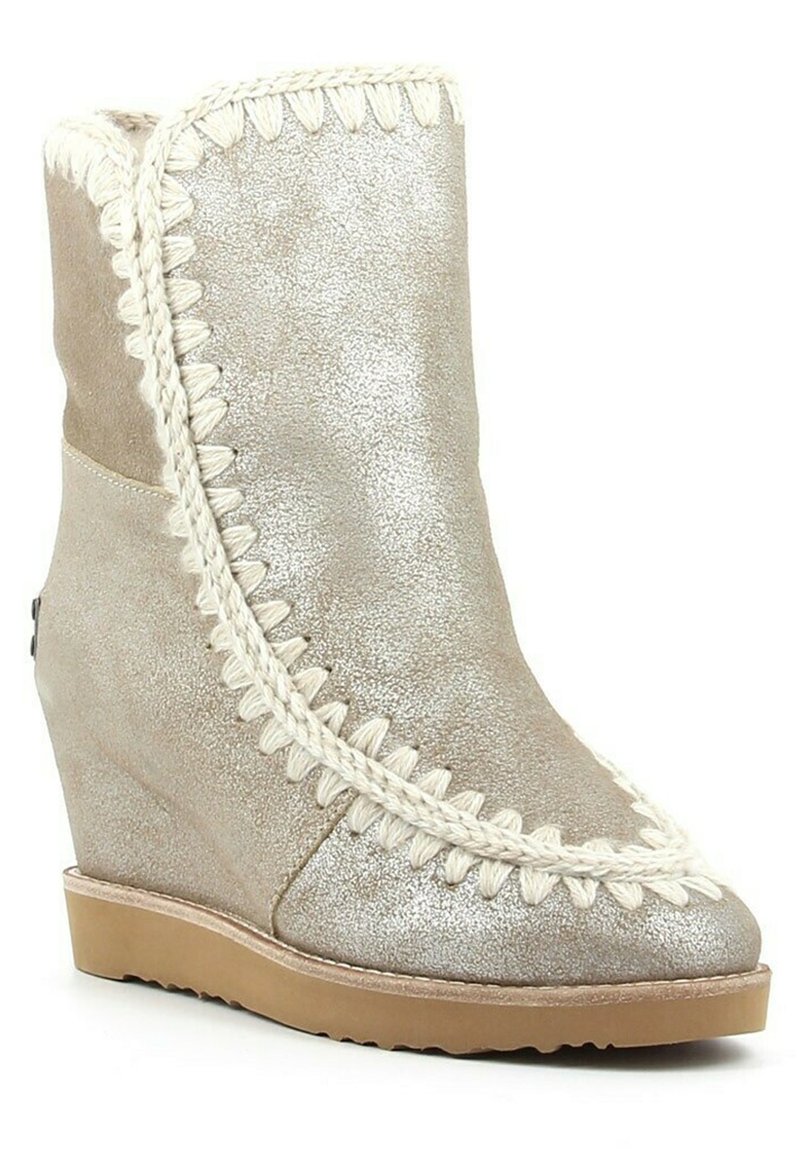 Beige wedge enkellaars met een gestructureerde afwerking, opvallende witte gevlochten rand langs de voorkant en bovenranden, en een lichtbruine zool.