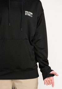 Haut à capuche noir avec cordons de serrage, poche avant et ourlet côtelé. Présente le logo "VOLCOM STONE" en blanc sur la poitrine gauche et des poignets avec ouverture pour le pouce.