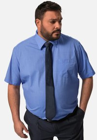 Camicia azzurra a maniche corte con colletto, tasca sul lato sinistro del petto, abbinata a una cravatta scura e pantaloni scuri. Tessuto morbido e vestibilità su misura.