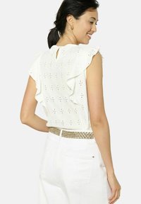 Top bianco a maniche corte con design delle spalle arricciato, in tessuto a bucchi e dettaglio a chiave sul retro del collo. Abbinato a pantaloni bianchi e una cintura intrecciata.