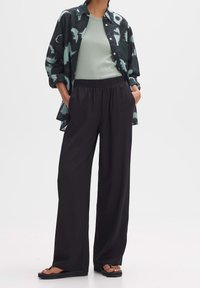 Svart och grön abstrakt mönstrad skjorta med knäppning, ljusgrön skjorta under, lösa svarta byxor, sandaler, avslappnad outfit, luftig passform.