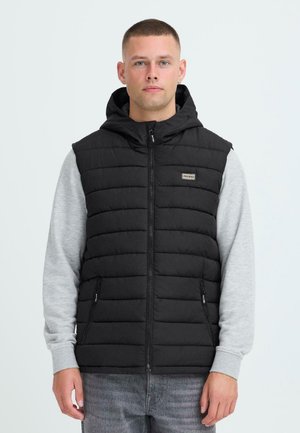 Gilet noir rembourré avec capuche, doté d'une fermeture éclair à l'avant, de deux poches latérales et d'un t-shirt à manches longues gris en dessous. Marquage discret sur la poitrine.