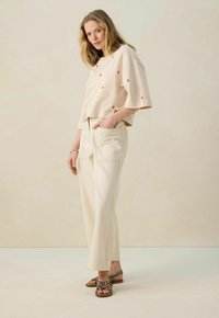 Crop top en maille beige avec des motifs orange, associé à un pantalon large crème et des sandales à imprimé léopard. Texture douce et coupe décontractée.