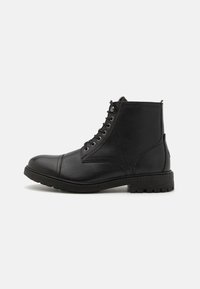 Botín de cuero negro hasta el tobillo con punta redonda, superficie texturizada, diseño con cordones, ojales de metal y una suela de goma resistente.