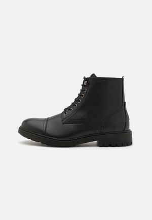 Botín de cuero negro hasta el tobillo con punta redonda, superficie texturizada, diseño con cordones, ojales de metal y una suela de goma resistente.