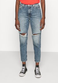 Light blue ripped jeans with a high waist, featuring a relaxed fit and frayed knee details, paired with black high-top sneakers.