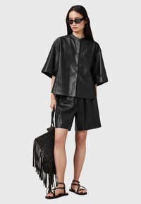 Black leather shirt with short sleeves, featuring front buttons and a rounded collar, paired with matching shorts and a woven black bag.