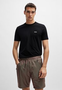 Camiseta negra de manga corta con un logo blanco de "BOSS" en el lado izquierdo del pecho; combinada con pantalones cortos marrones que tienen una cintura elástica y bolsillos laterales.