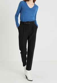 Blå långärmad tröja med v-ringning, tillsammans med högmidjade svarta byxor med bälte och sidfickor, bärs med vita ankelstövlar.