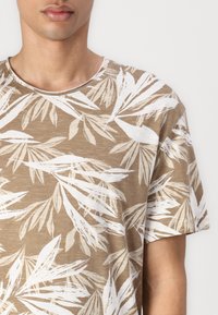 Brun kortærmet t-shirt med et hvidt bladmønster. Blød tekstur med rund hals og afslappet pasform, der viser subtile farvevariationer.