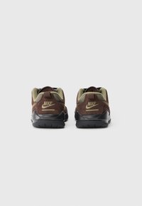 Brune semskede sneakers med sorte gummisåler, olivenfarvede accenter, og et fremtrædende Nike-logo på hælen og tungen. Strukturdesign.