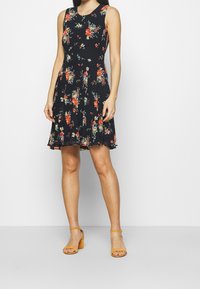 Robe florale en tissu noir, à design sans manches, silhouette en A, ornée de fleurs multicolores et d'un ourlet évasé.