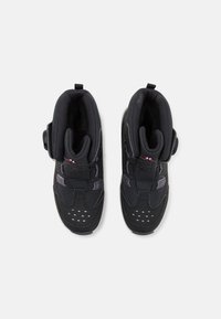 Baskets de sport noires avec un design montante, dotées d'un dessus texturé, de lacets et d'une fermeture à bouton rond pour un maintien sûr. Perforations blanches sur les orteils.