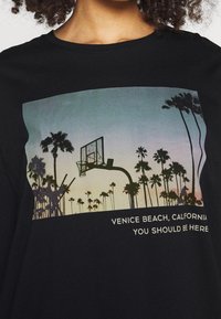 Czarny t-shirt z grafiką kosza do koszykówki na tle zachodu słońca i palm. Napis: „Venice Beach, Kalifornia, Powinieneś tu być.”