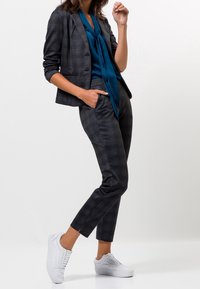 Conjunto de blazer y pantalones gris a cuadros, con una blusa azul verdosa con lazo, combinado con zapatillas blancas. Tejido suave, corte ajustado.